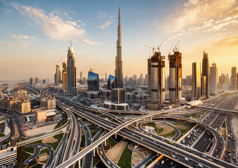 阿联酋迪拜壮观的天际线。一个大城市的未来主义现代建筑日落与一个大的高速公路交叉口。图片素材
