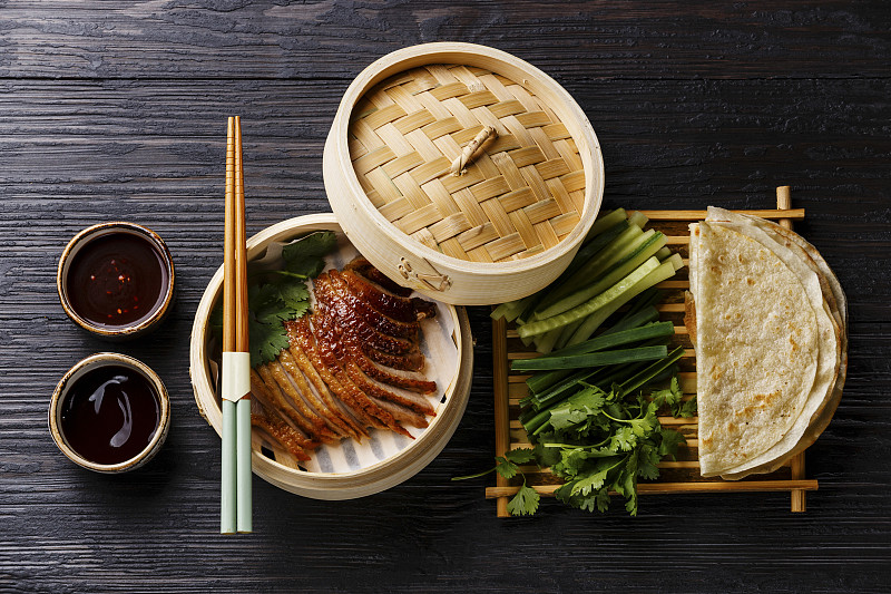 竹制蒸笼里的北京烤鸭配上新鲜的黄瓜、大葱、香菜和烤面饼，配上辣酱图片下载