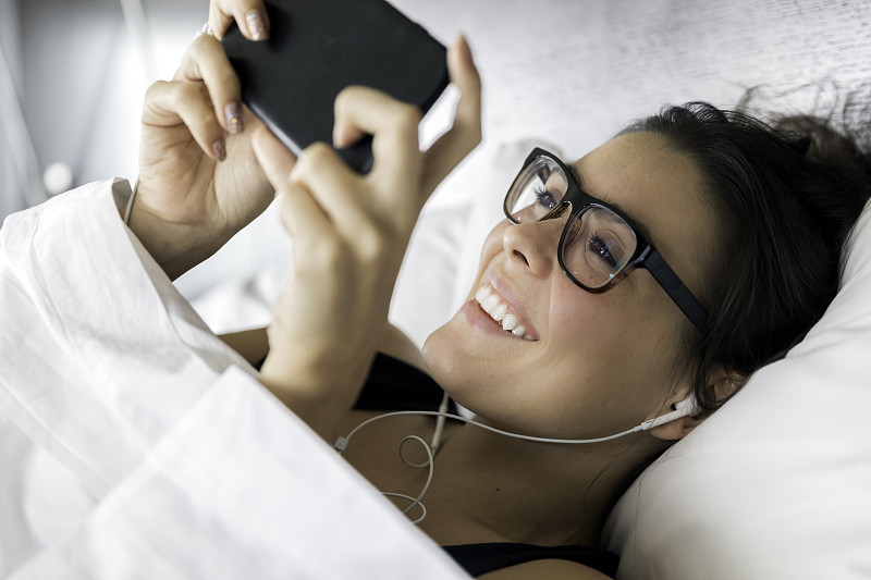 美丽的年轻女子在床上使用手机图片素材