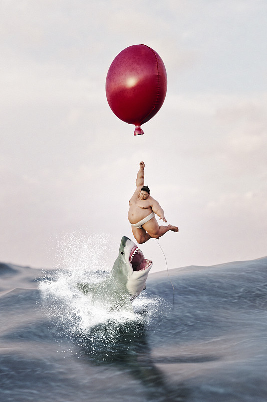 相扑手悬挂在海面上的气球上，大白鲨跃出水面图片下载