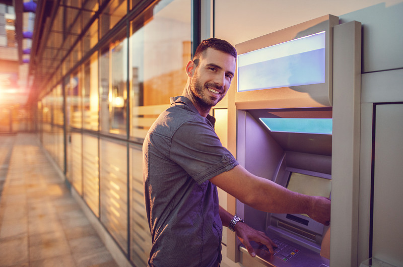 微笑的年轻商人从ATM机取款。图片下载