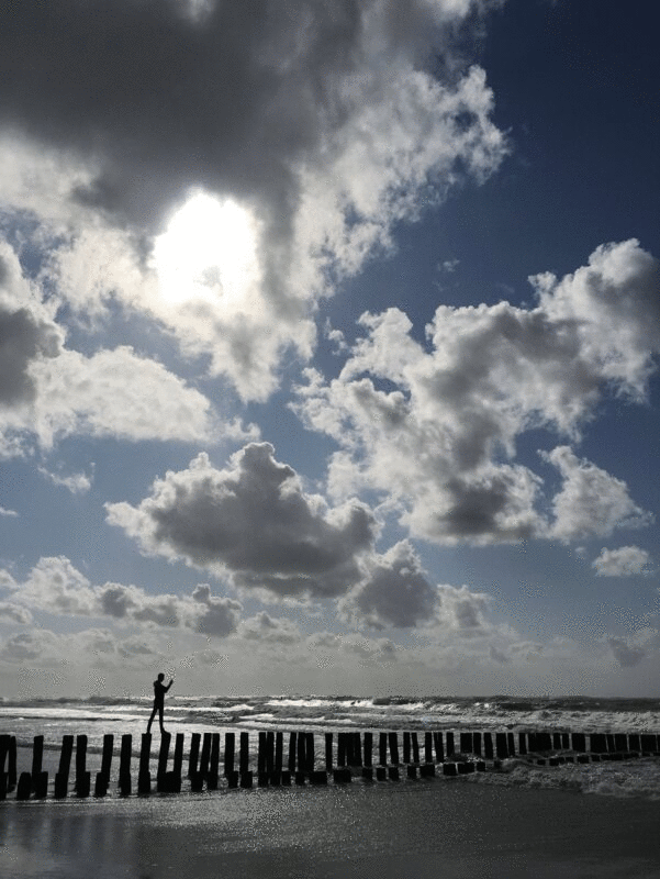 男子站在海滩上的旧码头塔上眺望大海的剪影图片下载