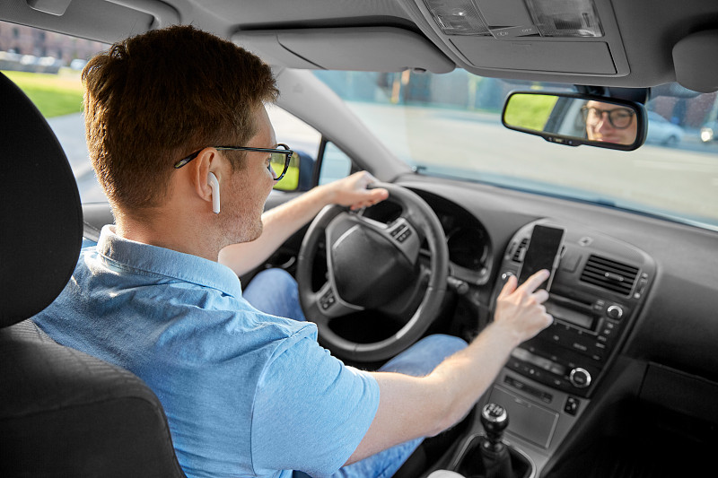 交通，车辆和人的概念-人或司机与无线耳机驾驶汽车和使用智能手机上的GPS导航。男人在开车，用智能手机上的GPS图片素材