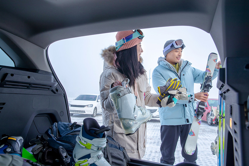 停车场内青年伴侣从汽车后备箱拿雪具图片素材