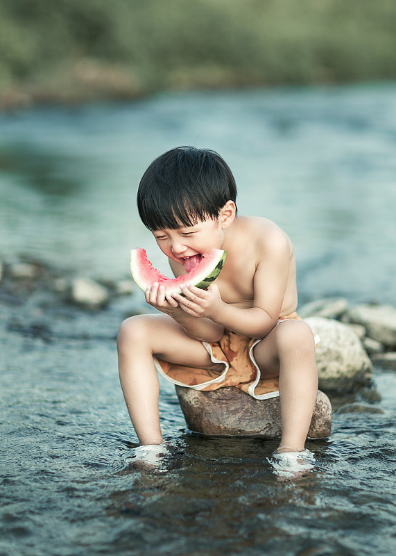夏天在河边吃西瓜玩水的小男孩图片下载