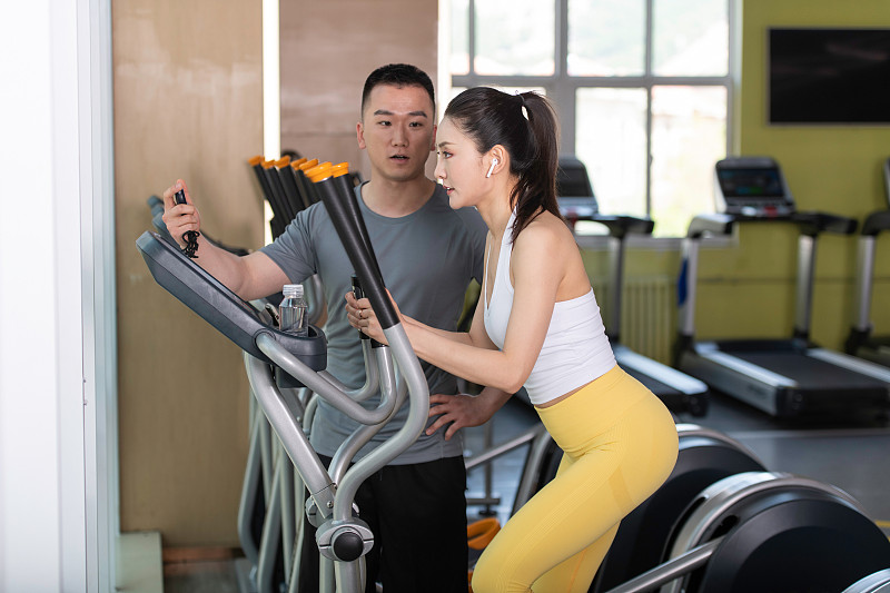 正在健身的年轻女性和男性，在健身房使用椭圆机锻炼。专业健身教练指导、评测和辅助训练、学习和交流。图片下载