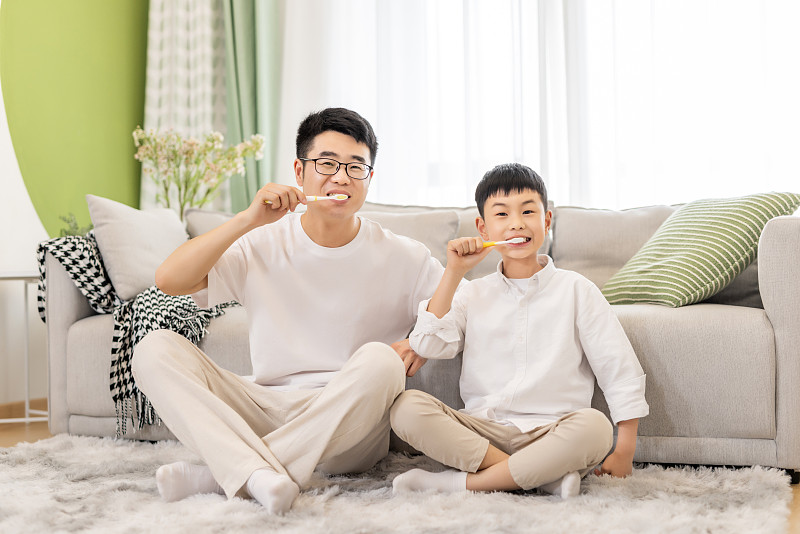 一对亚洲父子坐在客厅地毯上刷牙微笑图片下载