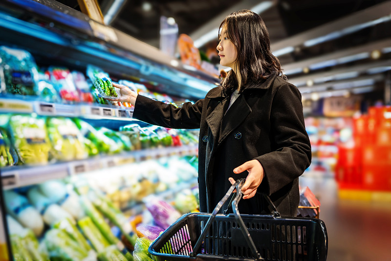 一名亚洲女孩在超市果蔬区挑选蔬菜图片下载