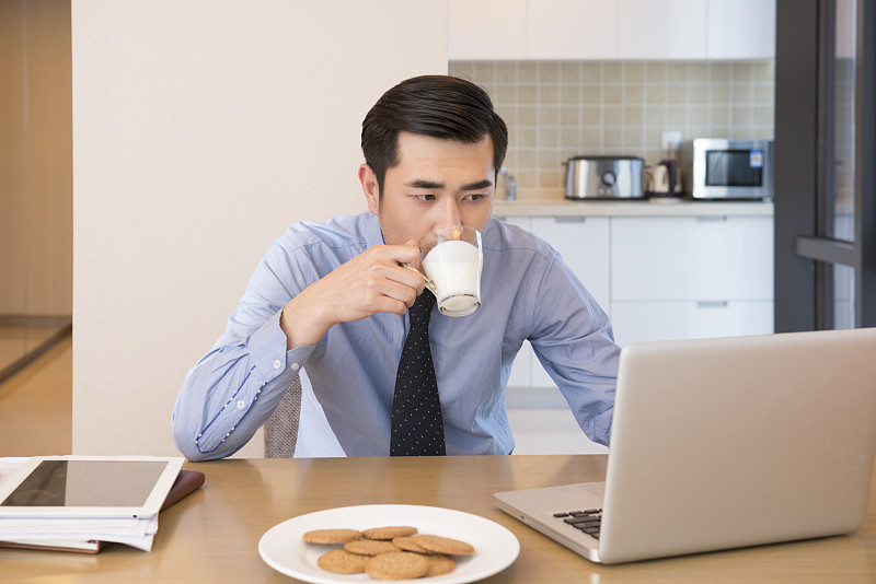 Young man using laptop at breakfast图片下载