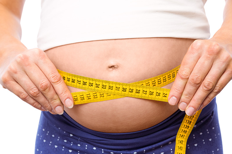 一名孕妇在白色背景下测量自己的肚子图片下载