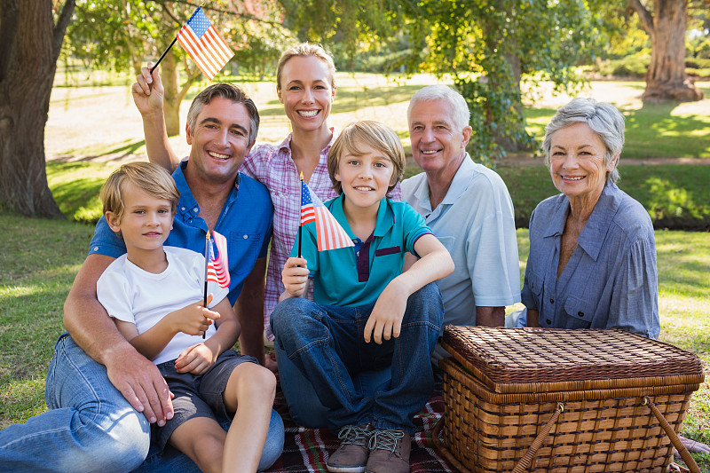 公园里快乐的一家人，在阳光明媚的日子里举着美国国旗图片下载