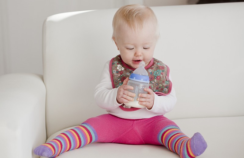 一个婴儿坐在沙发上，手里拿着一瓶牛奶图片下载