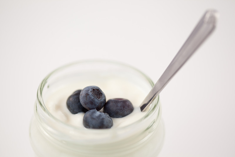 特写一罐酸奶与四个蓝莓对白色的背景图片下载