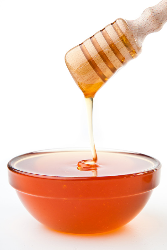 蜂蜜在白色的背景下滴落在碗里图片下载