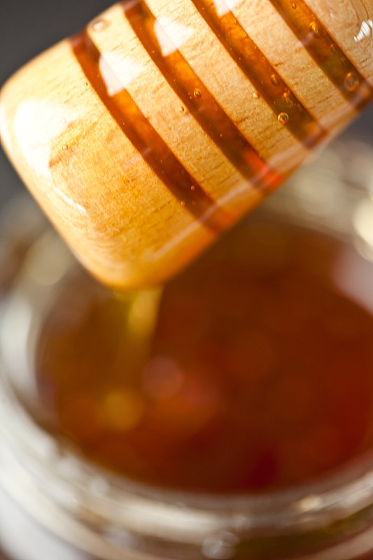 蜂蜜勺放在蜂蜜罐上，以黑色为背景图片下载