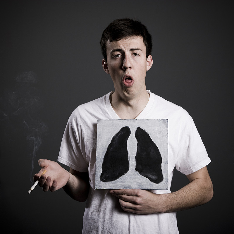 一个男人拿着一根点燃的香烟，在他的胸前举着一幅黑肺的画图片下载