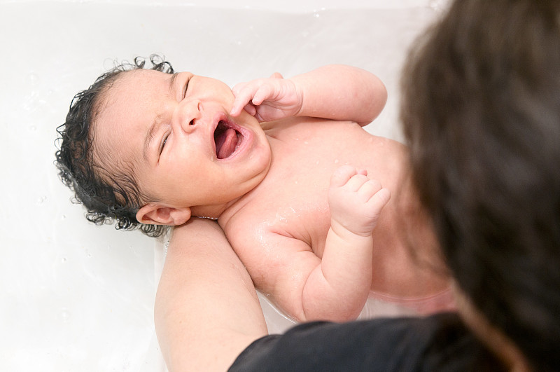 母亲在给哭闹的新生儿洗澡(1个月大)图片下载