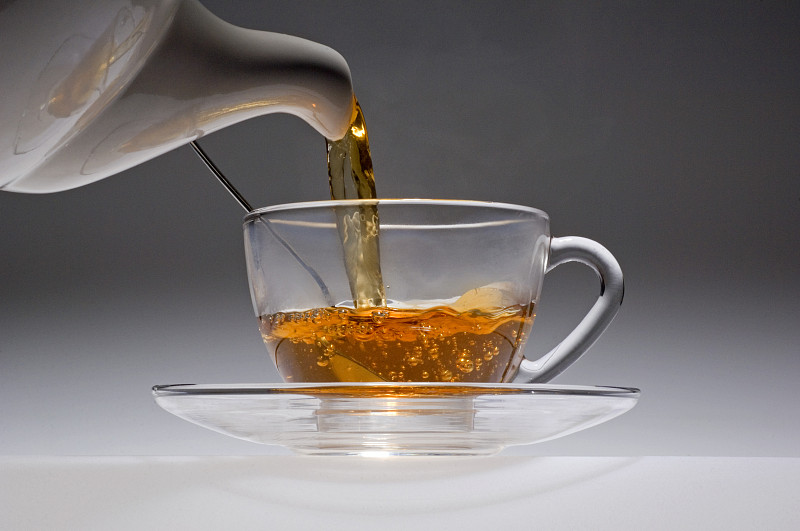 茶水从白色瓷壶倒入玻璃杯中。图片下载