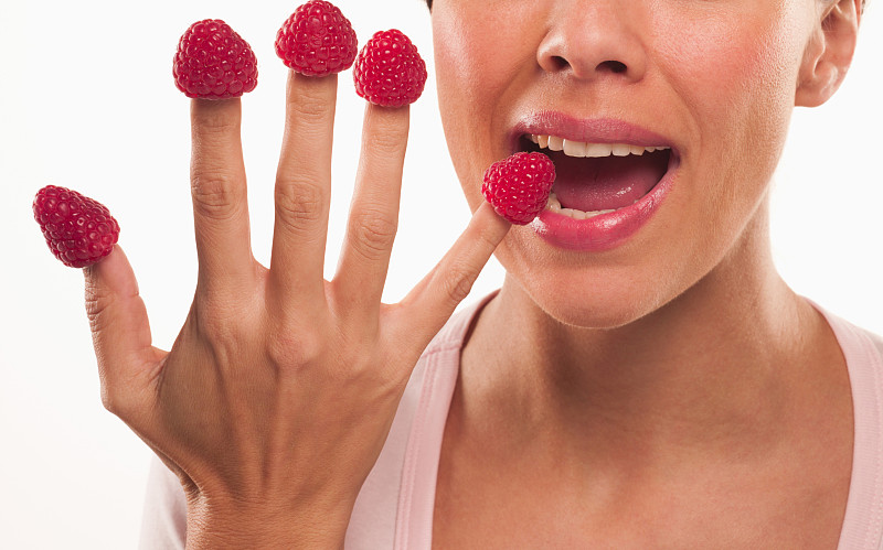 近距离的女人咬树莓的指尖图片下载