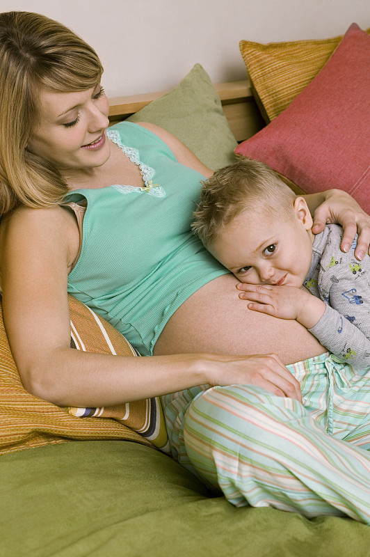 儿子(4-5)在床上枕着孕妇的肚子，肖像图片下载