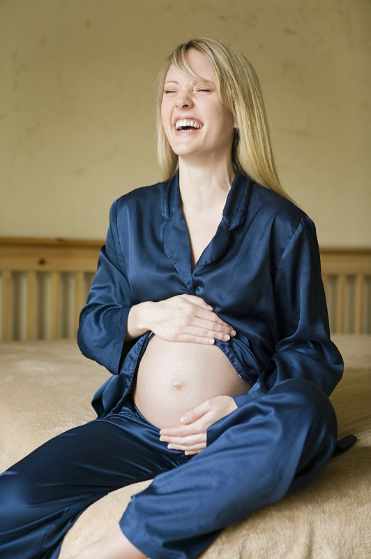 孕妇抱着肚子在卧室的床上笑图片下载