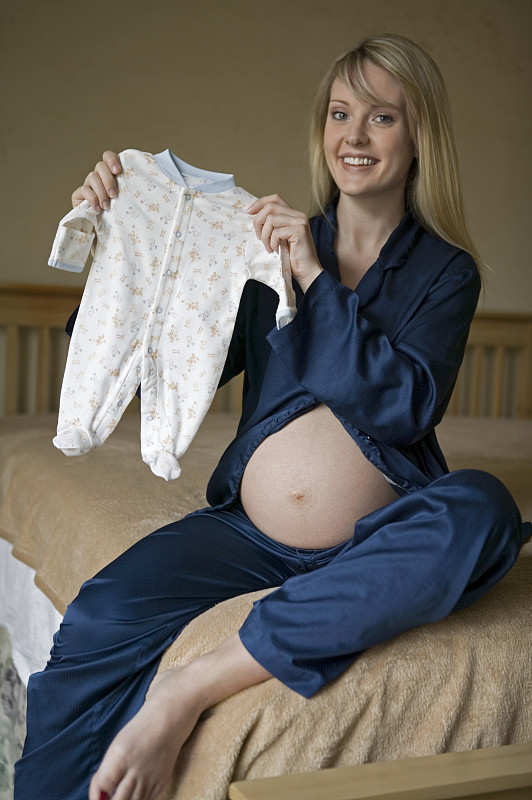 孕妇在卧室展示婴儿连体衣，肖像图片下载