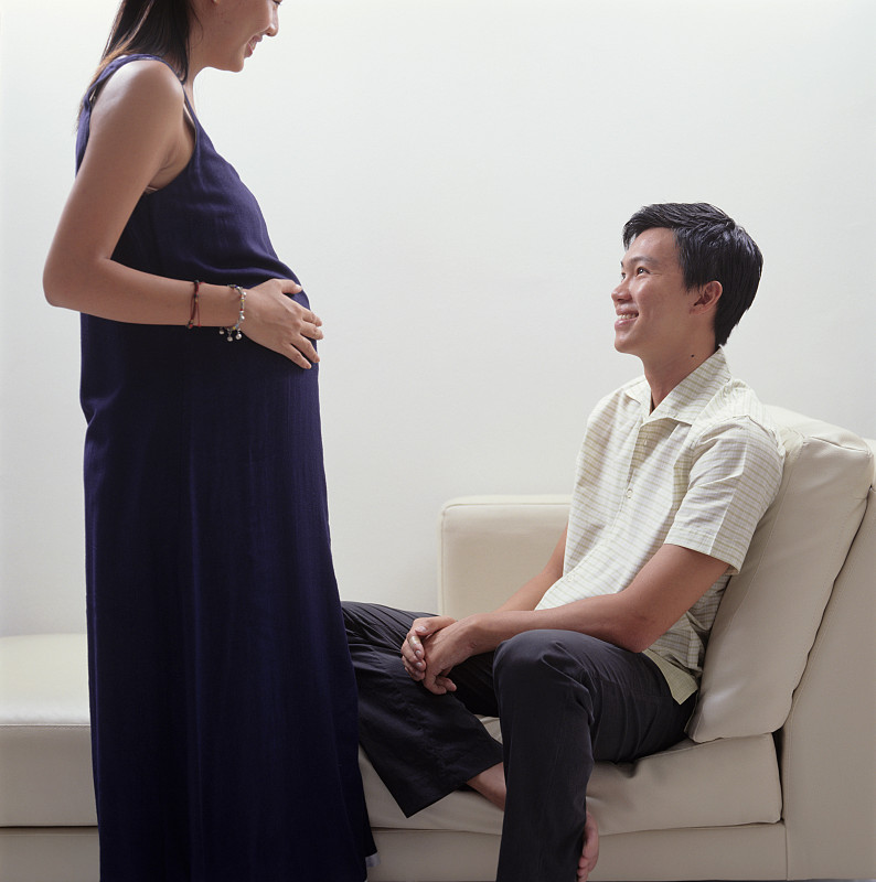 站着的孕妇和坐在沙发上的丈夫说话图片下载