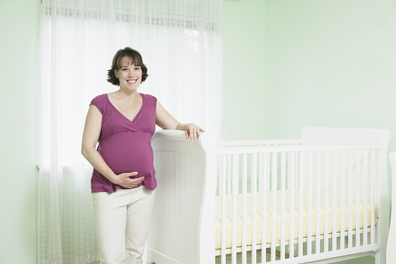 孕妇站在婴儿床旁，微笑，肖像图片下载