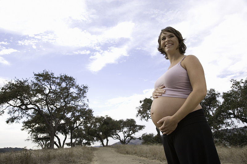 孕妇站在人行道上，手放在肚子上，侧视图片下载