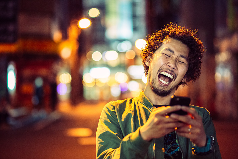 微笑的日本年轻人与智能手机在晚上的城市图片下载