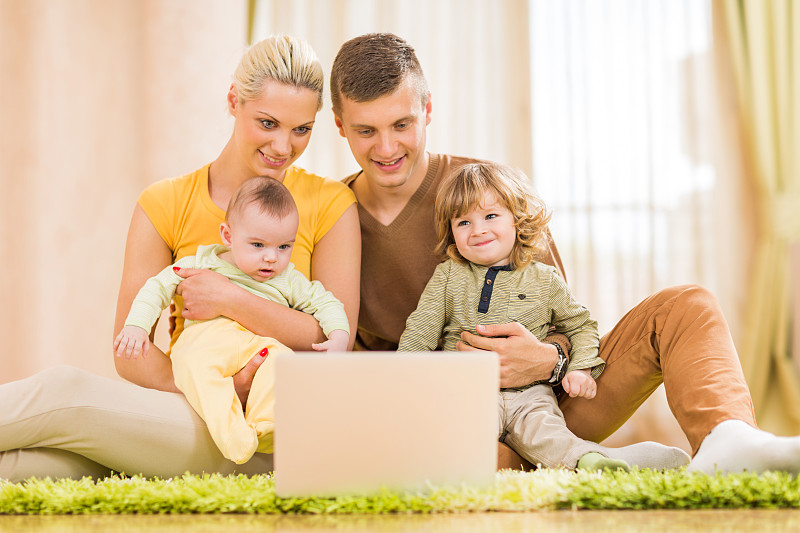 年轻的家庭坐在地毯上一起使用笔记本电脑。图片下载