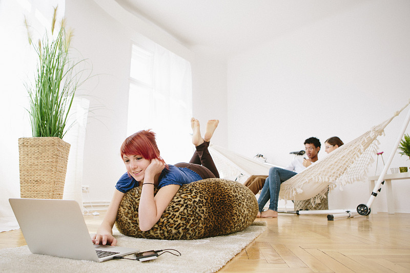 年轻的红发女人和朋友在吊床上玩笔记本电脑图片下载