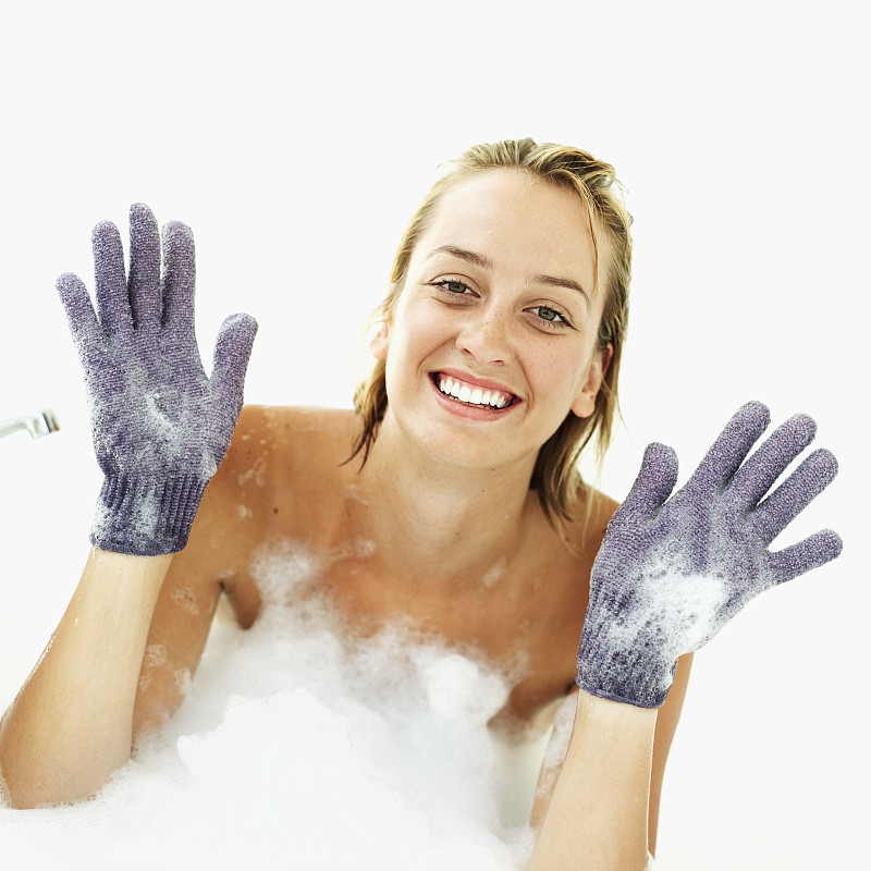 年轻女子戴着紫色丝瓜手套在泡泡浴中图片下载