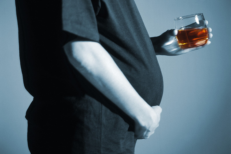 一个孕妇的特写镜头与手在她的boom和拿着啤酒的杯子图片下载