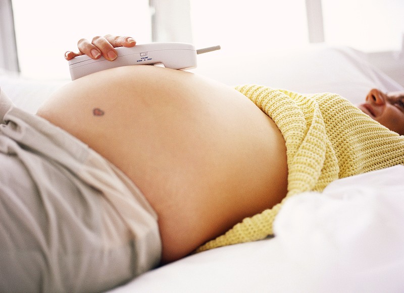 侧面特写的孕妇躺下与手机在她暴露的腹部图片下载