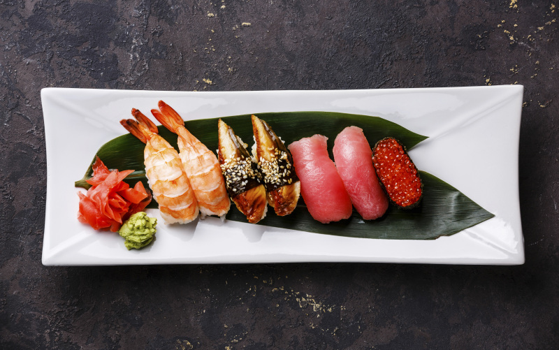 手握寿司和棒kan寿司放在白色盘子上，背景是黑色的图片下载