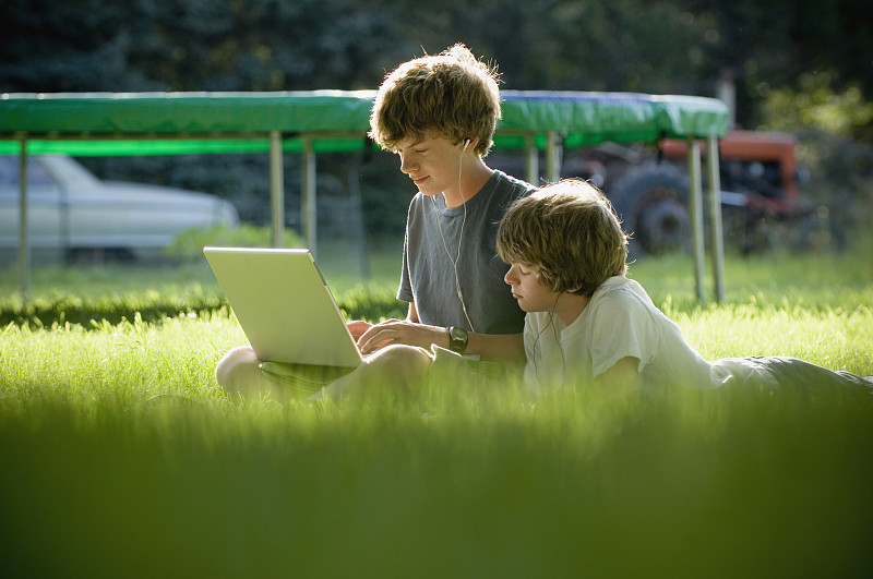 男孩们坐在草地上用笔记本电脑图片素材