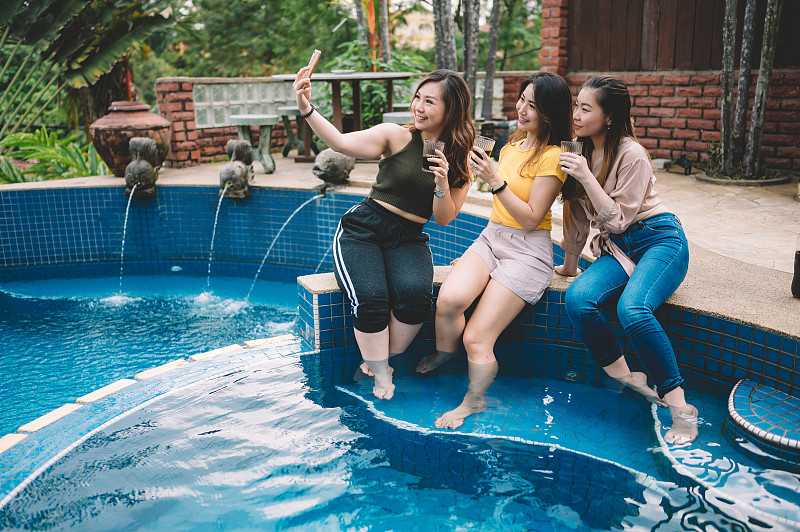 3名亚洲华人女性坐在泳池边享受下午的自拍图片下载