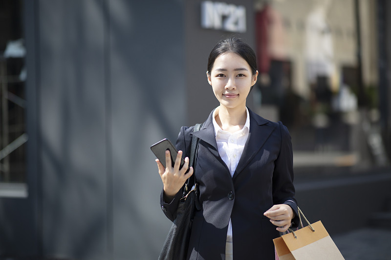 一名年轻女子在户外拿着智能手机拎着购物袋图片下载