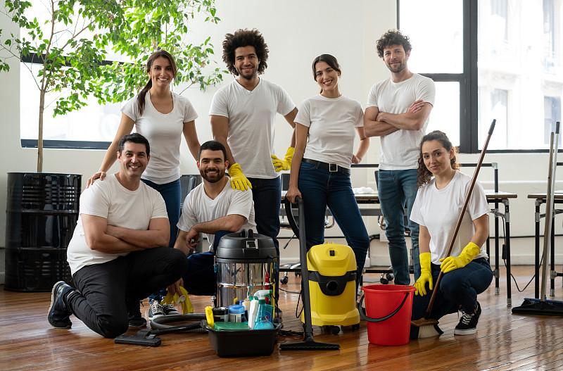 拉丁美洲多样化的清洁团队在一个办公室做一个微笑的镜头，同时拿着清洁设备图片素材