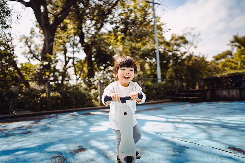 可爱的小亚洲学步女孩有乐趣和骑摩托车在公园快乐图片下载