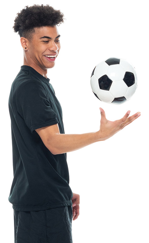 非洲裔年轻男性足球运动员站在白色背景前，穿着运动服，拿着足球，踢足球运动和使用运动球图片素材