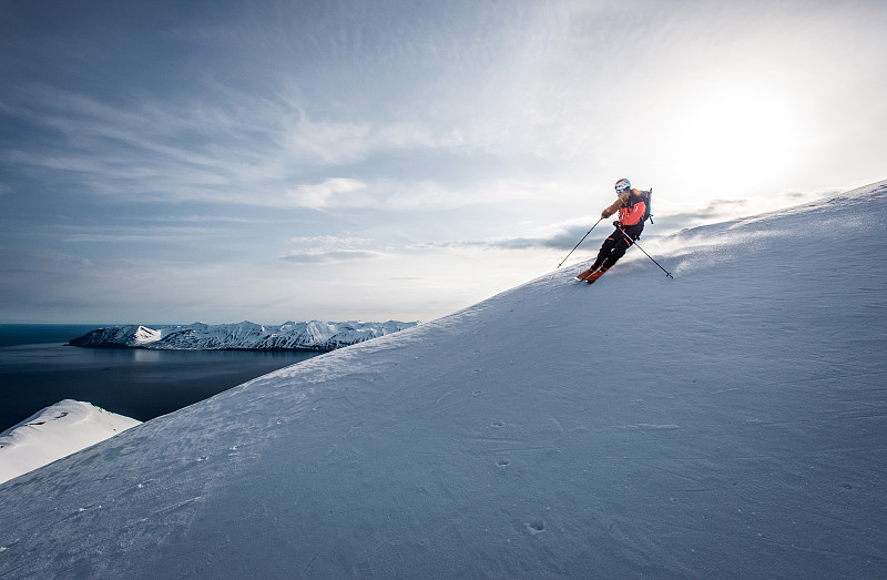在冰岛，一名男子以海洋为背景滑雪下山图片素材