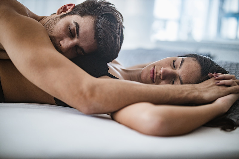 睡在床上的年轻夫妇手牵着手。图片下载
