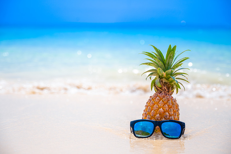 眼镜菠萝位于海边的海滩上，在炎热的阳光下，设置了夏季的概念。图片下载