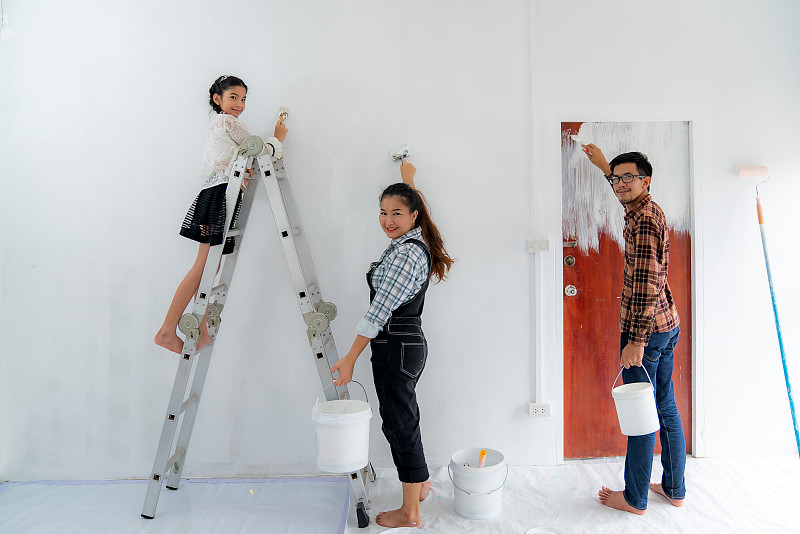 幸福的亚洲家庭与父亲，母亲和女儿在粉刷粉刷白色的墙壁在他们的新房子。家庭生活爱情关系，还是新房活动概念图片下载