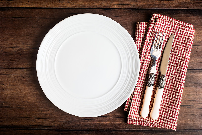空的白色盘子，刀叉餐巾在一个旧的木制棕色背景，俯视图。图像与复制空间。厨房桌子与毛巾和一个盘顶视图与复印空间。图片下载