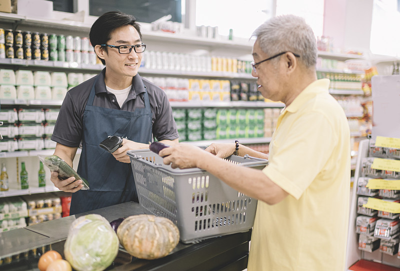 一位亚裔华人老人在超市柜台结账时向收银员付款图片下载