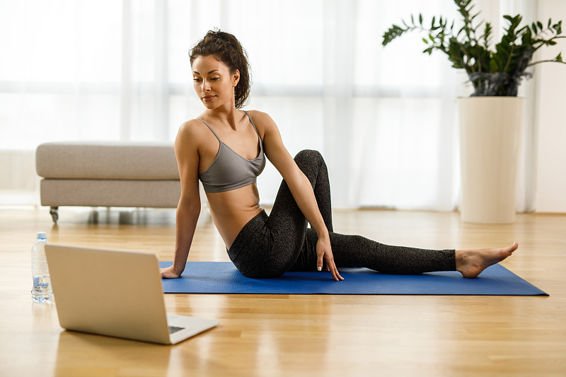 穿着运动服的女人一边练瑜伽，一边在笔记本电脑上看辅导课图片素材