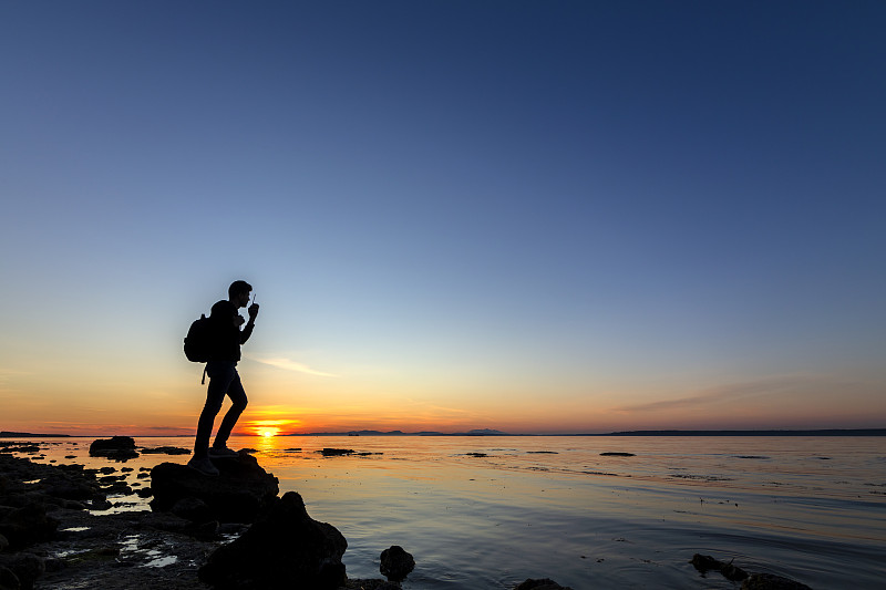 一个拿着步话机的人站在海边的岩石上图片下载